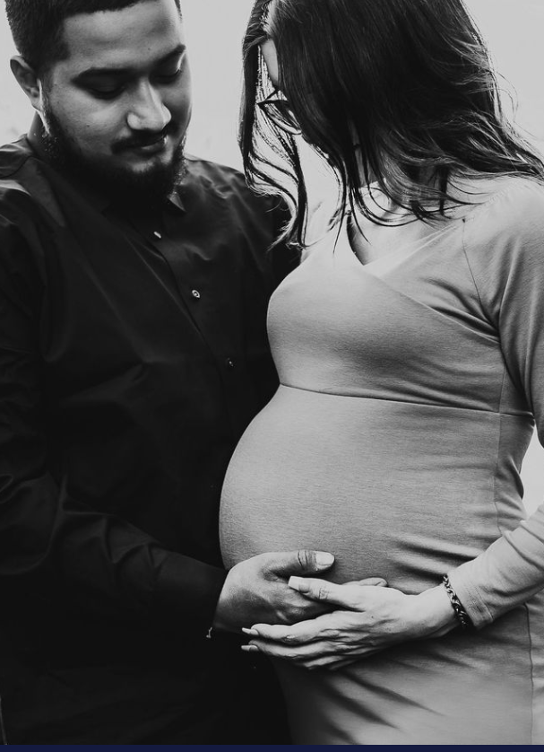 black and white photo of couple looking at pregnant belly